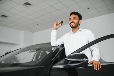 Smiling, friendly indian car seller standing in car salon