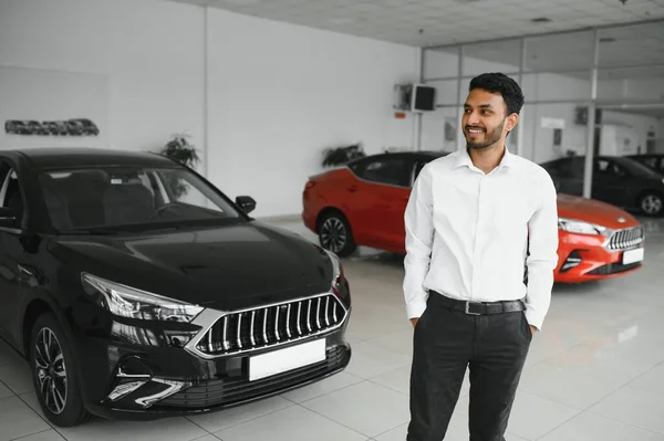 Smiling, friendly indian car seller standing in car salon