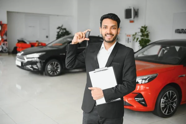 stock image Good looking, cheerful and friendly indian salesman poses in a car salon or showroom