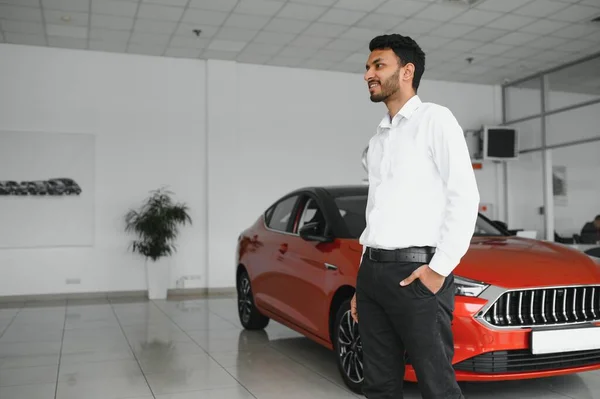Smiling, friendly indian car seller standing in car salon