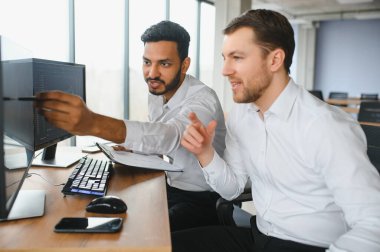 Two men traders sitting at desk at office together looking at data analysis discussing brainstorming successful strategy inspired teamwork concept close-up.