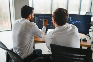 Ofiste oturan ve ekrana bakan iki başarılı tüccar, finans piyasası grafiğindeki kripto para birimi verilerini kontrol ediyor, monitöre işaret ediyor..