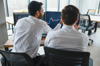 İki erkek tüccar ofiste birlikte oturmuş veri mumu grafiklerini izliyorlar. Fiyat akışını analiz ediyorlar. Gülümsüyorlar..