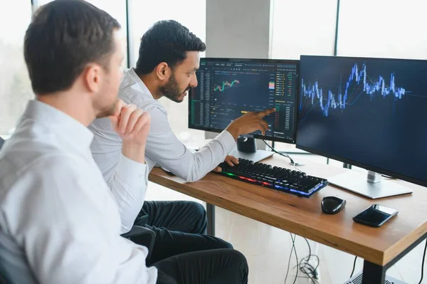 stock image Two diverse crypto traders brokers stock exchange market investors discussing trading charts research reports growth using pc computer looking at screen analyzing invest strategy, financial risks