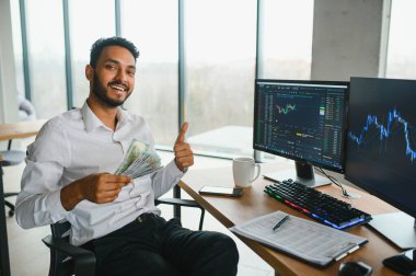 Young indian business man trader looking at computer screen with trading charts reflecting in eyeglasses watching stock trading market financial data growth concept, close up