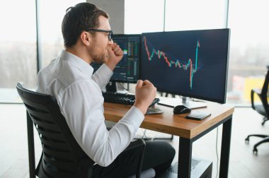 Man trader in formalwear sitting at desk in frot of monitors with charts and data at office