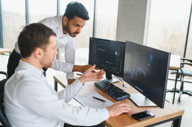 Ofiste oturan ve ekrana bakan iki başarılı tüccar, finans piyasası grafiğindeki kripto para birimi verilerini kontrol ediyor, monitöre işaret ediyor..