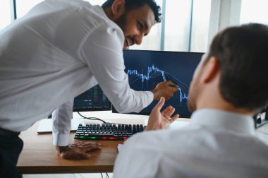 Ofiste oturan ve ekrana bakan iki başarılı tüccar, finans piyasası grafiğindeki kripto para birimi verilerini kontrol ediyor, monitöre işaret ediyor..