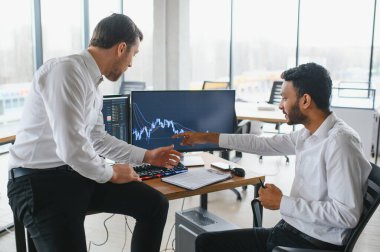 Two successful trader in formalwear pointing at display, analyzing stat and dynamic on forex charts, working in office together.