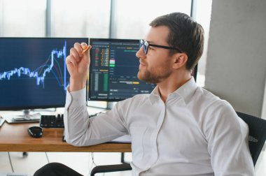 Man trader in formalwear sitting at desk in frot of monitors with charts and data at office