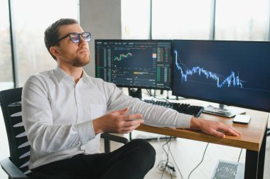 Man trader in formalwear sitting at desk in frot of monitors with charts and data at office