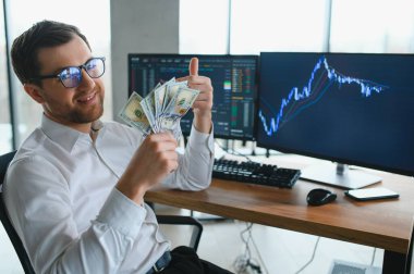 Man trader in formalwear sitting at desk in frot of monitors with charts and data at office