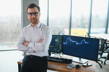 Man trader in formalwear sitting at desk in frot of monitors with charts and data at office