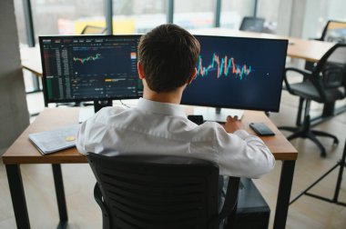 Man trader in formalwear sitting at desk in frot of monitors with charts and data at office