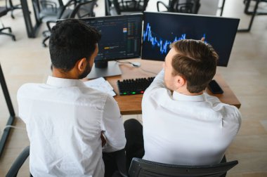 Ofiste oturan ve ekrana bakan iki başarılı tüccar, finans piyasası grafiğindeki kripto para birimi verilerini kontrol ediyor, monitöre işaret ediyor..