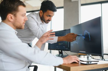 Two men traders sitting at desk at office together monitoring stocks data candle charts on screen analyzing price flow smiling cheerful having profit teamwork concept. clipart