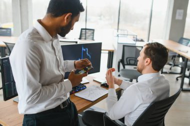 Two successful trader in formalwear pointing at display, analyzing stat and dynamic on forex charts, working in office together.