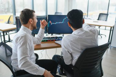 Ofiste oturan ve ekrana bakan iki başarılı tüccar, finans piyasası grafiğindeki kripto para birimi verilerini kontrol ediyor, monitöre işaret ediyor..