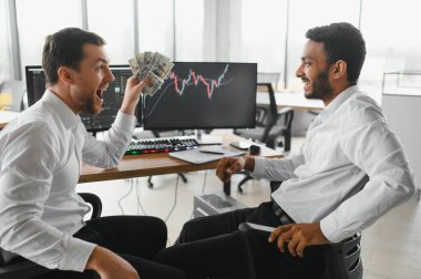Two men traders sitting at desk at office together monitoring stocks data candle charts on screen analyzing price flow smiling cheerful having profit teamwork concept.