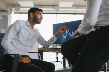 Two successful trader in formalwear pointing at display, analyzing stat and dynamic on forex charts, working in office together.