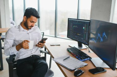 Düşünceli, konsantre Hintli iş adamı yatırımcı yönetici bilgisayar kullanıyor, web sitesinde veri pazarını analiz ediyor ve dizüstü bilgisayara bakarak web araştırması yapıyor.