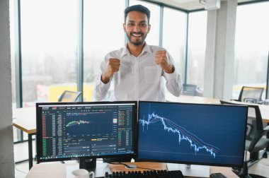 Young indian business man trader looking at computer screen with trading charts reflecting in eyeglasses watching stock trading market financial data growth concept, close up