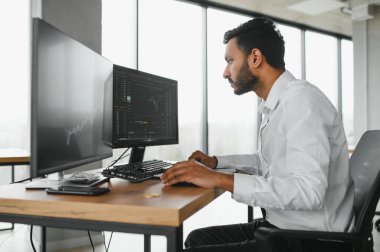 Akıllı Hintli kripto tüccarı, yatırımcı, analist bilgisayar ve akıllı telefon kullanarak dijital kripto döviz borsasını, borsa grafiklerini, yatırım yapmayı düşünme ve fon risklerini analiz ediyor.