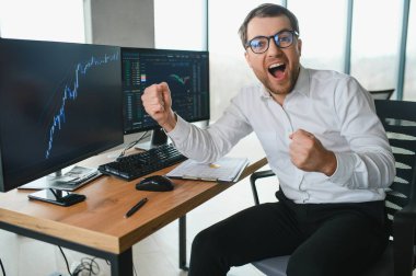 Man trader in formalwear sitting at desk in frot of monitors with charts and data at office