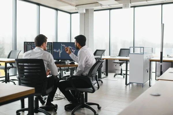 stock image Two men traders sitting at desk at office together monitoring stocks data candle charts on screen analyzing price flow smiling cheerful having profit teamwork concept.