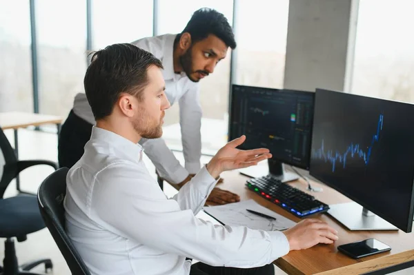 stock image Two diverse crypto traders brokers stock exchange market investors discussing trading charts research reports growth using pc computer looking at screen analyzing invest strategy, financial risks