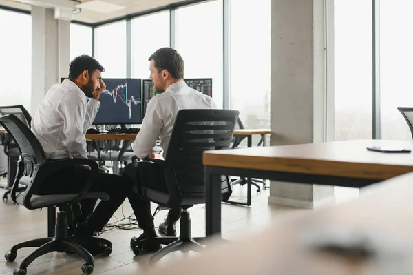 stock image Two men traders sitting at desk at office together monitoring stocks data candle charts on screen analyzing price flow smiling cheerful having profit teamwork concept.
