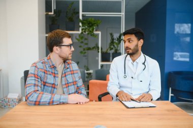 medicine, healthcare and people concept - indian doctor young male patient meeting at hospital.