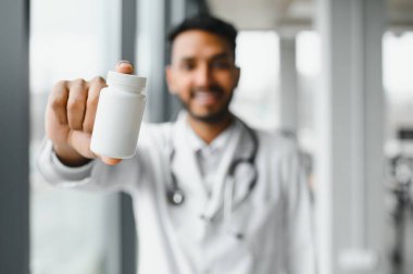 Handsome Indian Male Doctor holding empty white or blank dropper bottle.