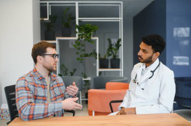 medicine, healthcare and people concept - indian doctor young male patient meeting at hospital.