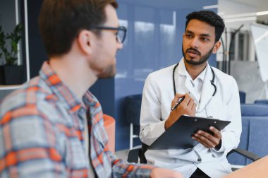 Indian doctor in white gown seeing patients in office