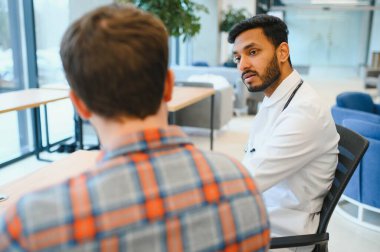 Indian doctor in white gown seeing patients in office