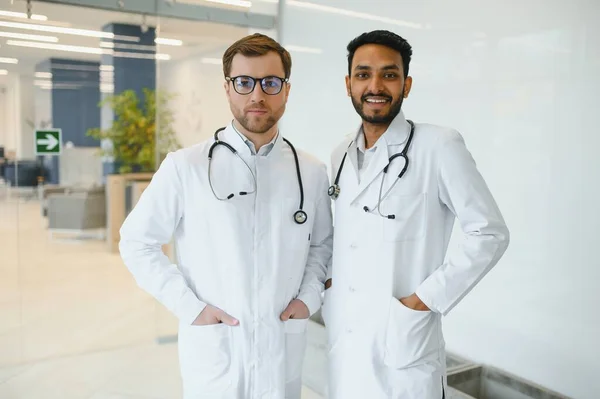 An Indian doctor and a European doctor stand together in a hospital lobby