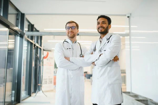 An Indian doctor and a European doctor stand together in a hospital lobby