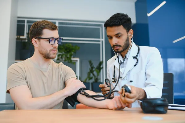 Indian Doctor Holding Dial While Measuring Man's Blood Pressure.