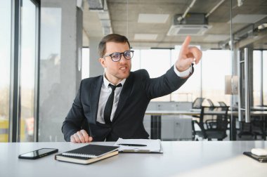 Angry businessman sitting at his desk and screaming at his employees