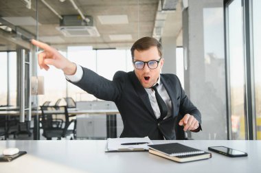Angry businessman sitting at his desk and screaming at his employees