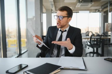 Angry businessman sitting at his desk and screaming at his employees