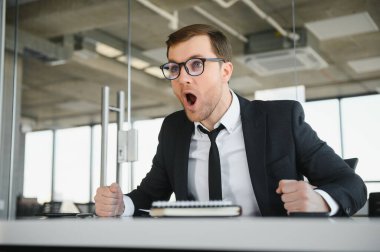 Angry businessman sitting at his desk and screaming at his employees