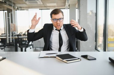 Angry businessman sitting at his desk and screaming at his employees