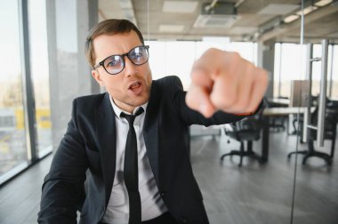 Angry businessman sitting at his desk and screaming at his employees