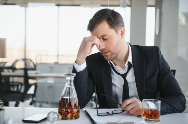 Alcoholism at work. Tired employee drinking alcohol at workplace, can not handle stress