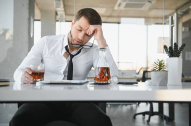 Alcoholism at work. Tired employee drinking alcohol at workplace, can not handle stress