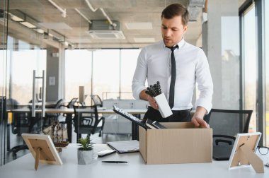 Fired young man packing his stuff in office. clipart