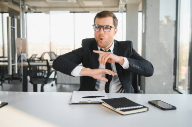 Angry businessman sitting at his desk and screaming at his employees