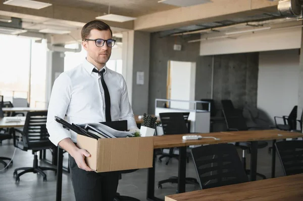 stock image Young handsome businessman in light modern office with carton box. Last day at work. Upset office worker is fired